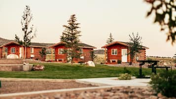 Une rangée de chalets en rondins, avec une pelouse verdoyante et des arbres en arrière-plan.