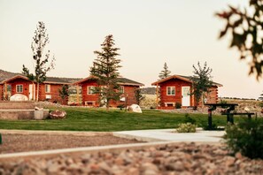 A row of log cabins with a grassy lawn and trees in the background.