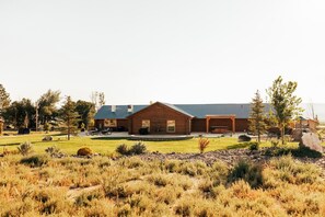 A log cabin with a patio and outdoor seating area, surrounded by a landscaped yard with rocks and shrubs.