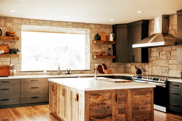 A modern kitchen with a large island, stone walls, wooden cabinets, and a built-in stove.