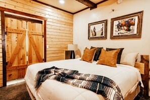 A bedroom with a wooden door, a bed with multiple pillows, and two framed pictures on the wall.