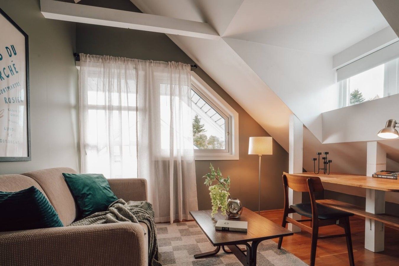 A cozy loft-style living space with a high ceiling, a dining area, and a large window with sheer curtains.