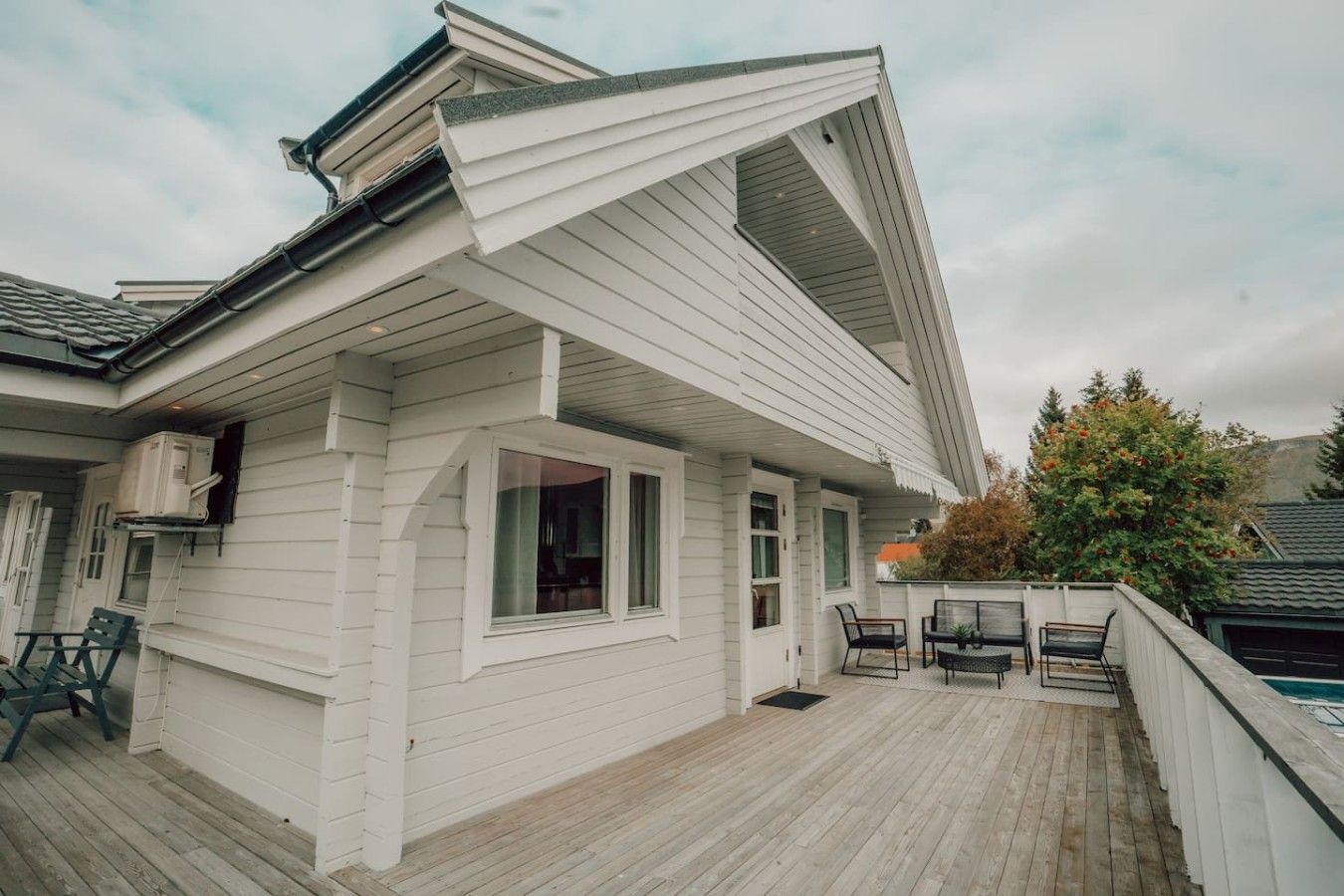 A white house with a sloped roof, a covered deck, and a pool.