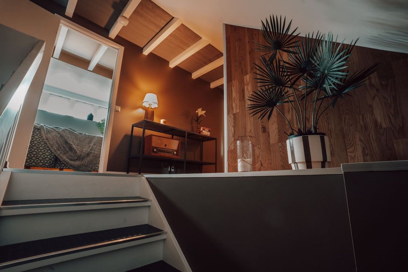 A staircase leading to a room with a wooden wall, a lamp, and a potted plant.