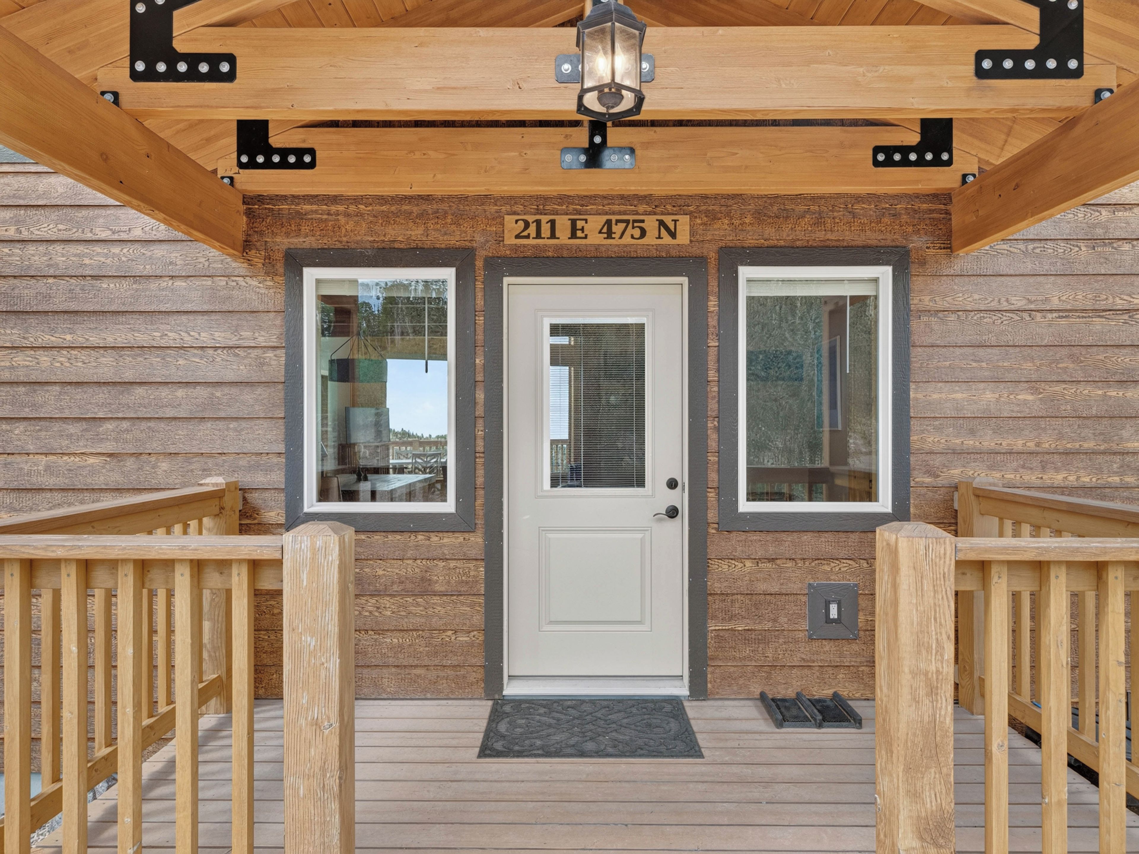 A wooden exterior with a white door, two windows, and a wooden deck with railings.