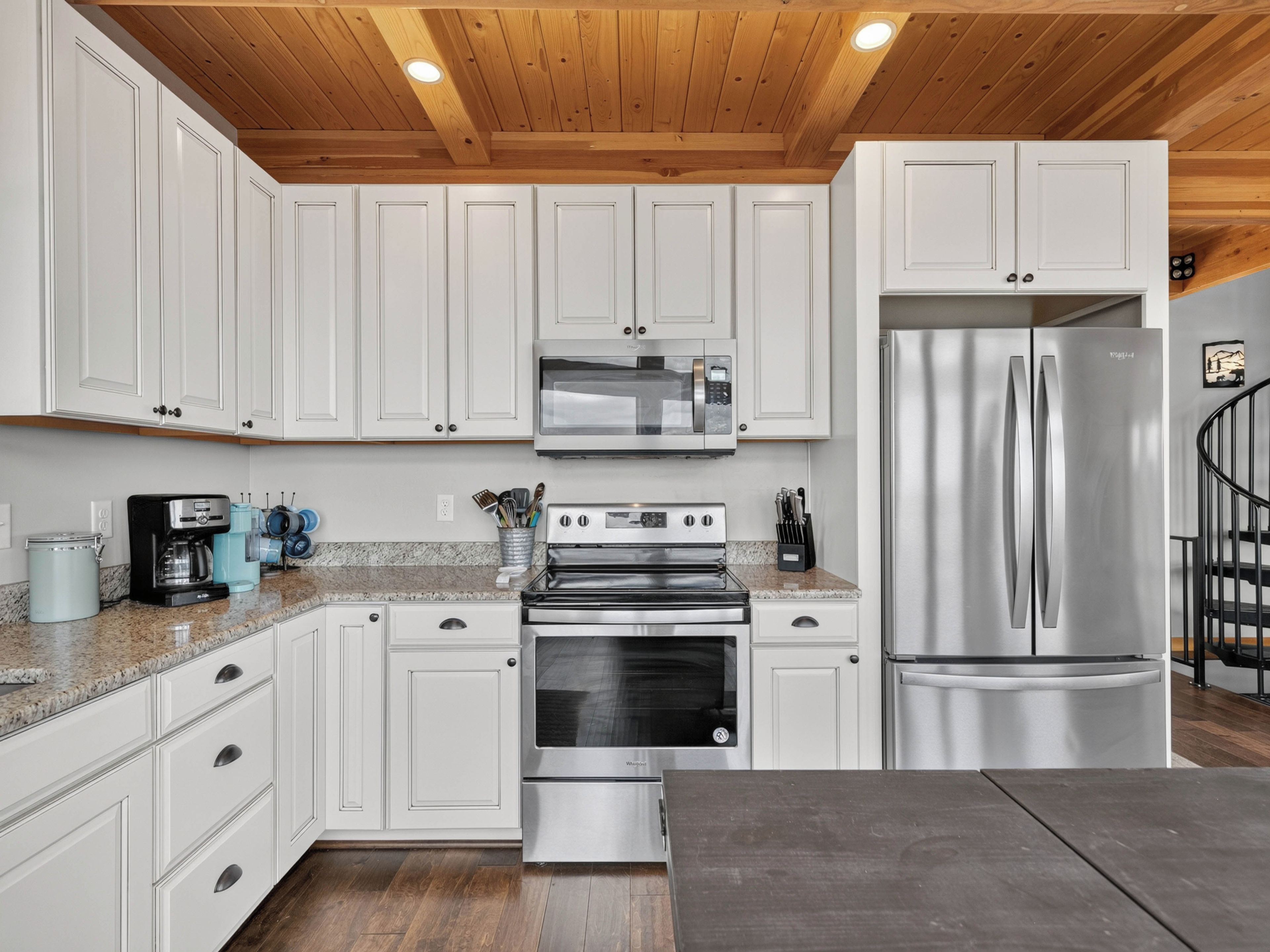 A modern kitchen with white cabinets, stainless steel appliances, and a wooden ceiling.