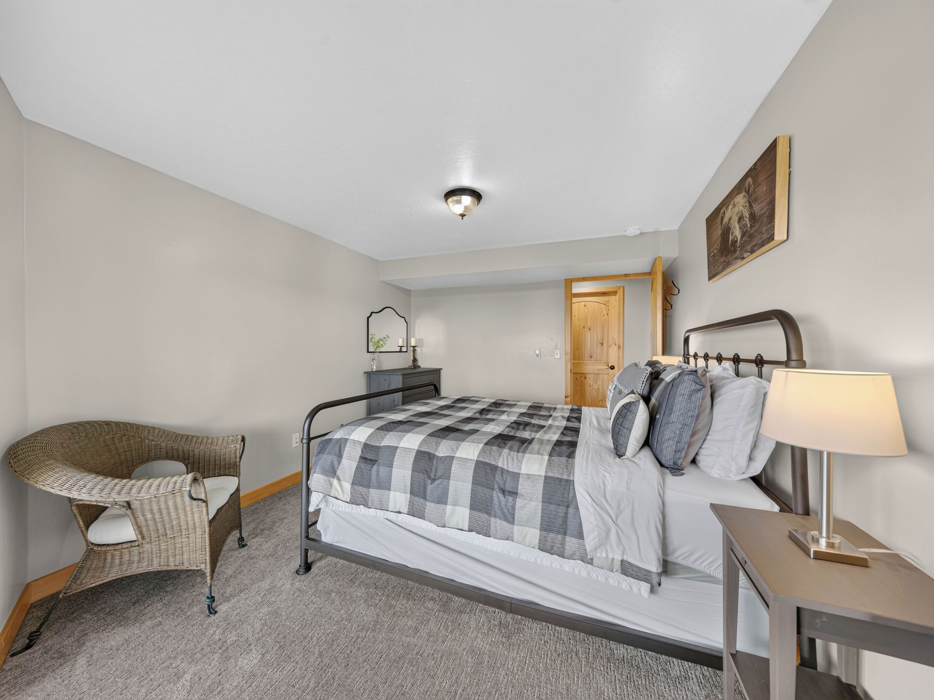 A bedroom with a bed, a chair, a bedside table, a lamp, a door, and a painting on the wall.