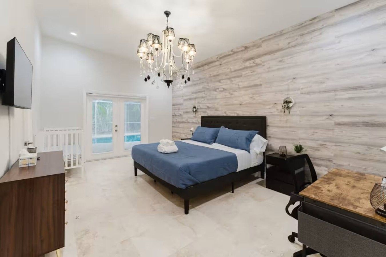 A bedroom with a bed, a chandelier, a television, and a view of a pool through a glass door.