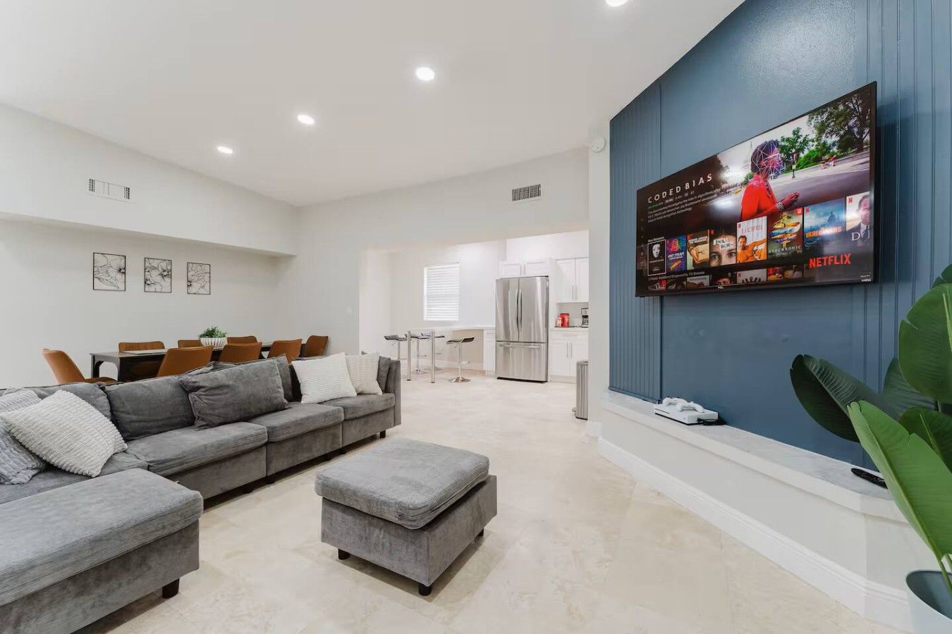 Un salon moderne avec un canapé d’angle gris, un pouf gris et un téléviseur à écran plat fixé à un mur bleu.