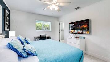 Ein Schlafzimmer mit Bett, Schreibtisch, Stuhl, Fernseher und Deckenventilator.