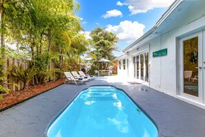 A swimming pool with lounge chairs, surrounded by greenery and a building with glass doors. - 5BD House - Pool+BBQ+King beds | 3 min to beach (Hollywood)