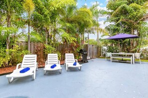 A patio area with white lounge chairs, a wooden table, and a purple umbrella. - 5BD House - Pool+BBQ+King beds | 3 min to beach (Hollywood)