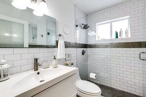 A modern bathroom with white subway tiles, a large mirror, a shower with a handheld showerhead, and a toilet. - 5BD House - Pool+BBQ+King beds | 3 min to beach (Hollywood)