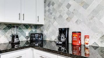 A kitchen with white cabinets, a granite countertop, a blender, a coffee maker, and two coffee containers.