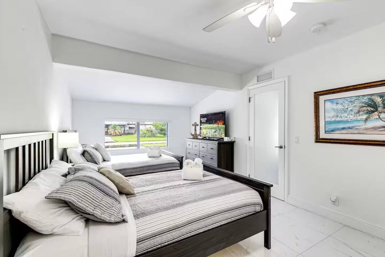 A bedroom with a bed, a nightstand, a dresser, a television, and a painting.