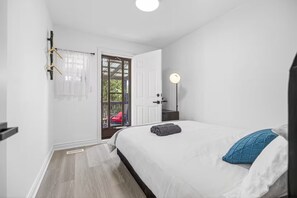 Un dormitorio con cama, mesita de noche, lámpara, puerta que da a un área exterior y ventana con cortinas.