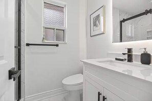 Un baño con inodoro blanco, lavamanos con grifo negro y espejo sobre el lavamanos.