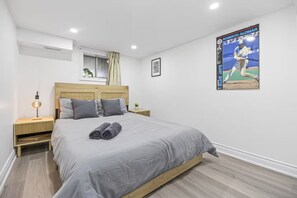 Un dormitorio con cama, mesitas de noche, aire acondicionado instalado en la pared, una ventana con cortinas y un cartel de deportes.