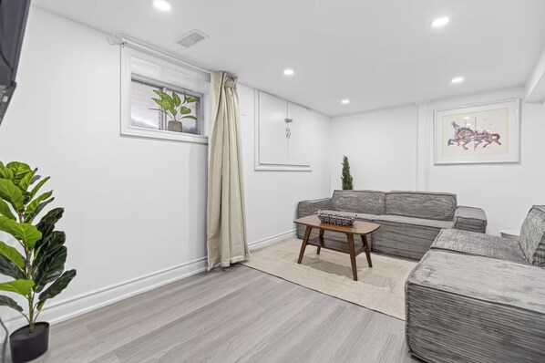 Una sala moderna con un sofá gris, una pequeña mesa de centro de madera y una planta en maceta.