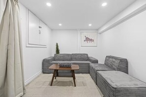 Una sala moderna con un sofá seccional, una mesita de madera y un cuadro en la pared.