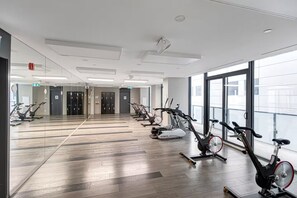 Una palestra con cyclette e uno specchio lungo tutta la parete, pavimento in legno e ampie finestre.