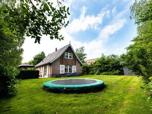 A house with a triangular roof, a front porch, and a trampoline in the yard. - Holiday Home With 2 Bedrooms (Appelscha)