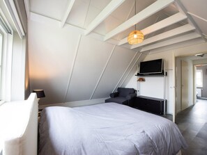 A modern bedroom with a sloped ceiling, a bed, a desk, and a television mounted on the wall. - Holiday Home With 2 Bedrooms (Appelscha)