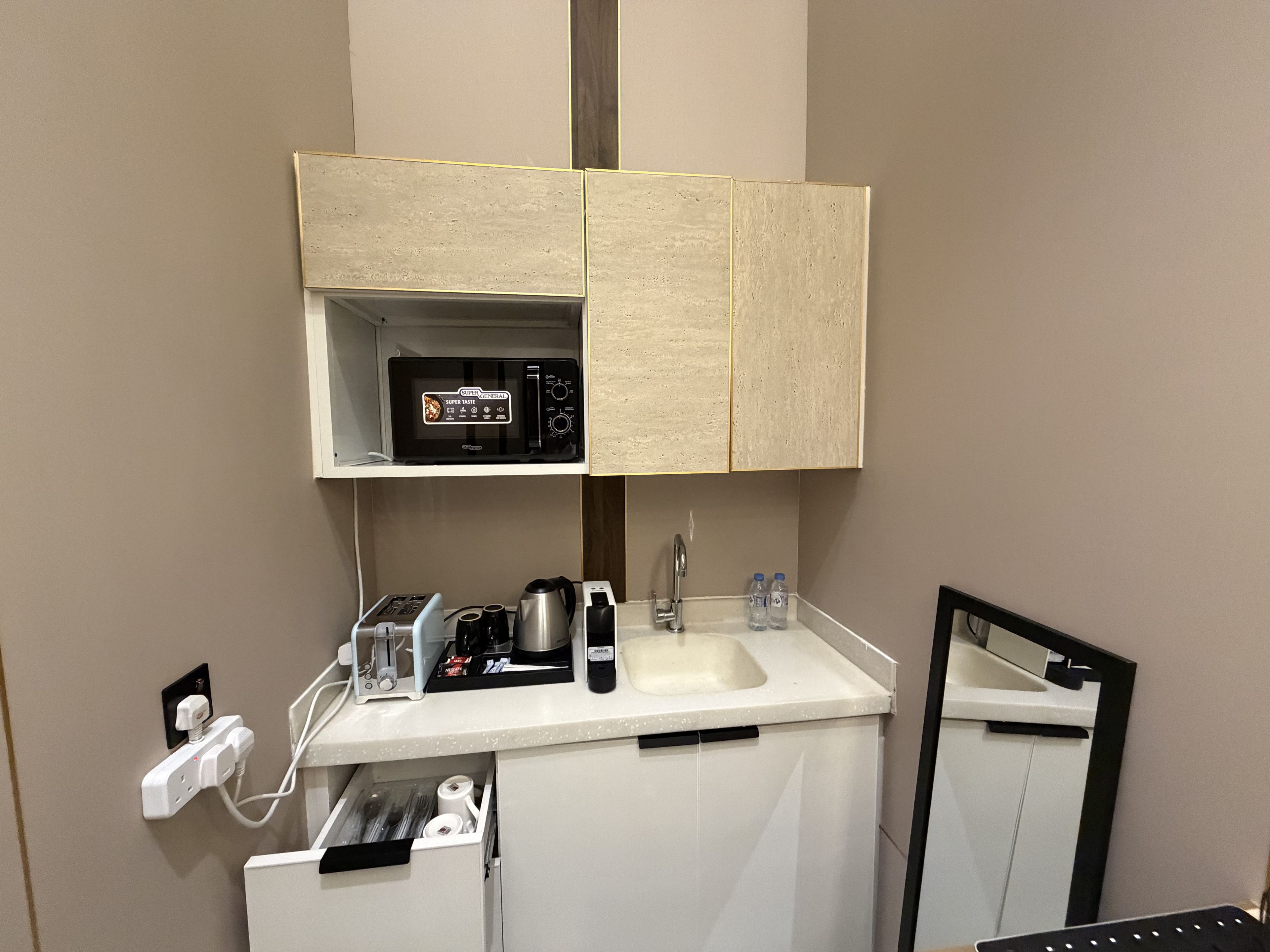 Un baño con mostrador blanco, microondas integrado, lavamanos y espejo.