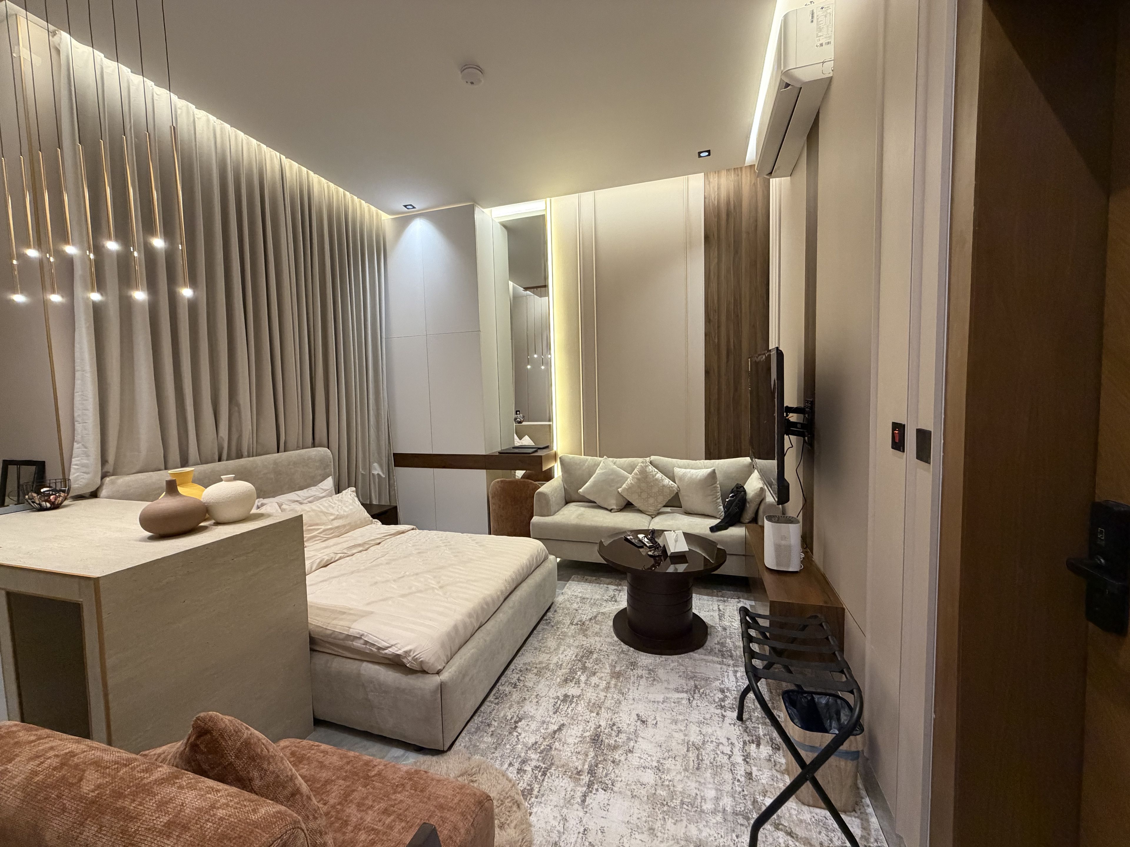 Quarto de hotel moderno com cama, sofá e uma pequena área de jantar.