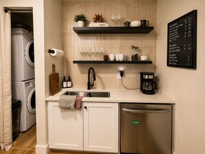 Eine kompakte Küche mit einer eingebauten Waschmaschine, einer Kaffeemaschine und einem 'CLEAN'-Hinweis am Kühlschrank.