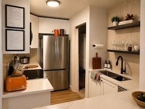 A modern kitchen with a stainless steel refrigerator, a toaster, and a sink. There are framed documents on the wall and a shelf with glasses and a plant. - Retro Park City Condo, 3BR + Loft, Near Major Ski Resorts (Park City)
