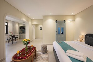 A hotel room with a bed, a bedside table with a vase of flowers, a small table with a drink, and a view of the kitchen and dining area. - Cozy Stay at bait assel by spacey  (cairo)