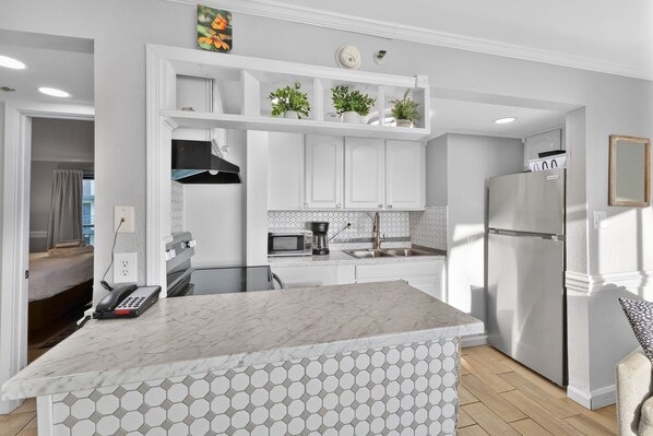 A modern kitchen with white cabinetry, a marble countertop, and a built-in oven. - Monterey Bay 1437 - Ocean Front (Myrtle Beach)