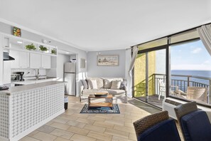 A modern kitchen with white cabinets, a dining area with a white sofa and a coffee table, and a balcony with a view of the sea. - Monterey Bay 1437 - Ocean Front (Myrtle Beach)