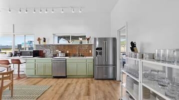 A modern kitchen with a stainless steel refrigerator, a dishwasher, and a microwave. There is a dining area with a table and chairs.