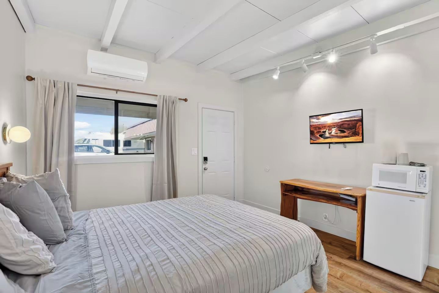 A bedroom with a bed, a desk, a microwave, and a painting on the wall.
