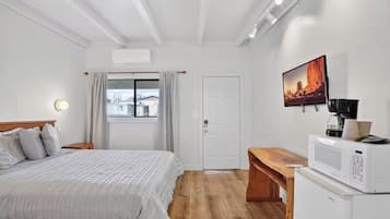 A hotel room with a bed, a wooden bench, a microwave, a coffee maker, and a painting on the wall.