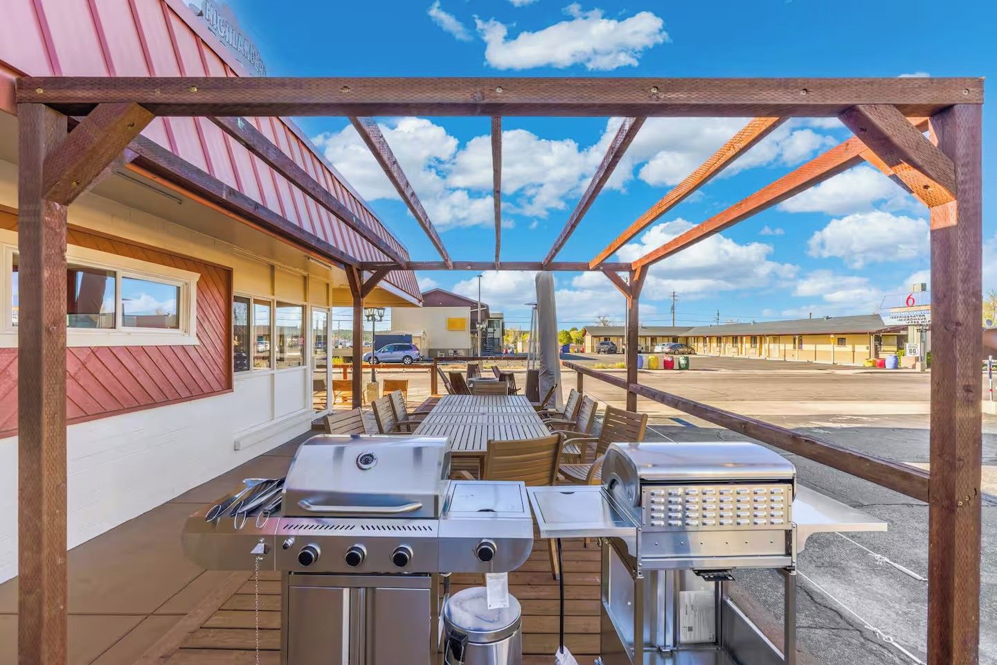 An outdoor patio with a grill, seating, and a view of a motel in the background.