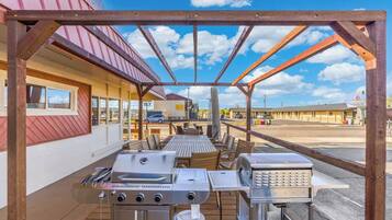 An outdoor patio with a grill, seating, and a view of a motel in the background.