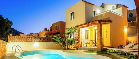 A residential property with a swimming pool, outdoor seating, and a well-lit patio area.