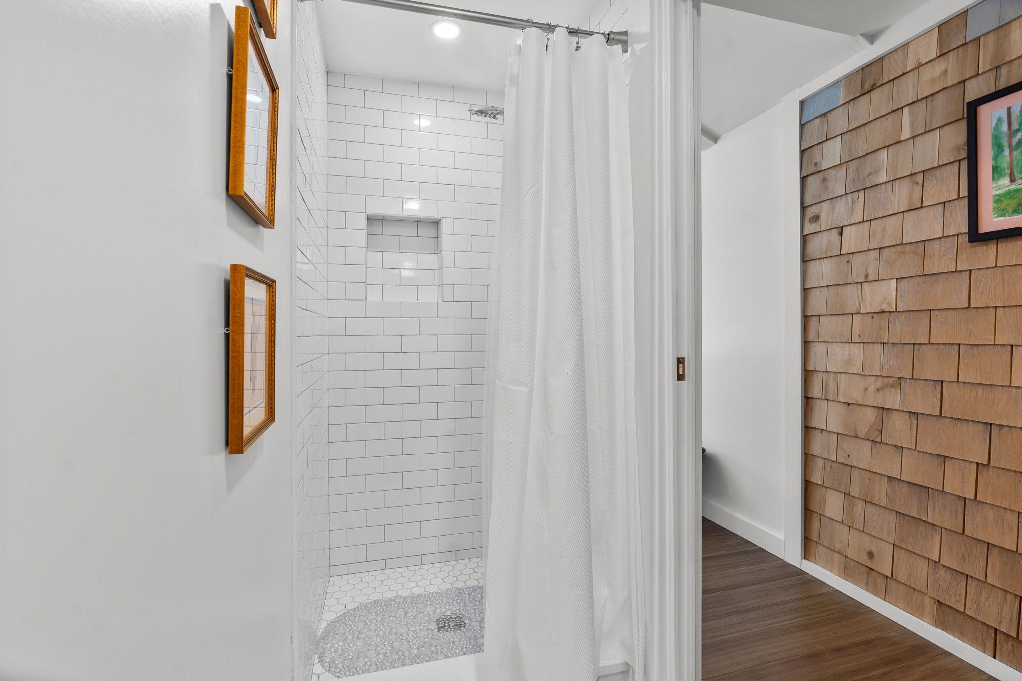 A modern bathroom with white tiled walls, a shower area, and a wooden wall with a picture.