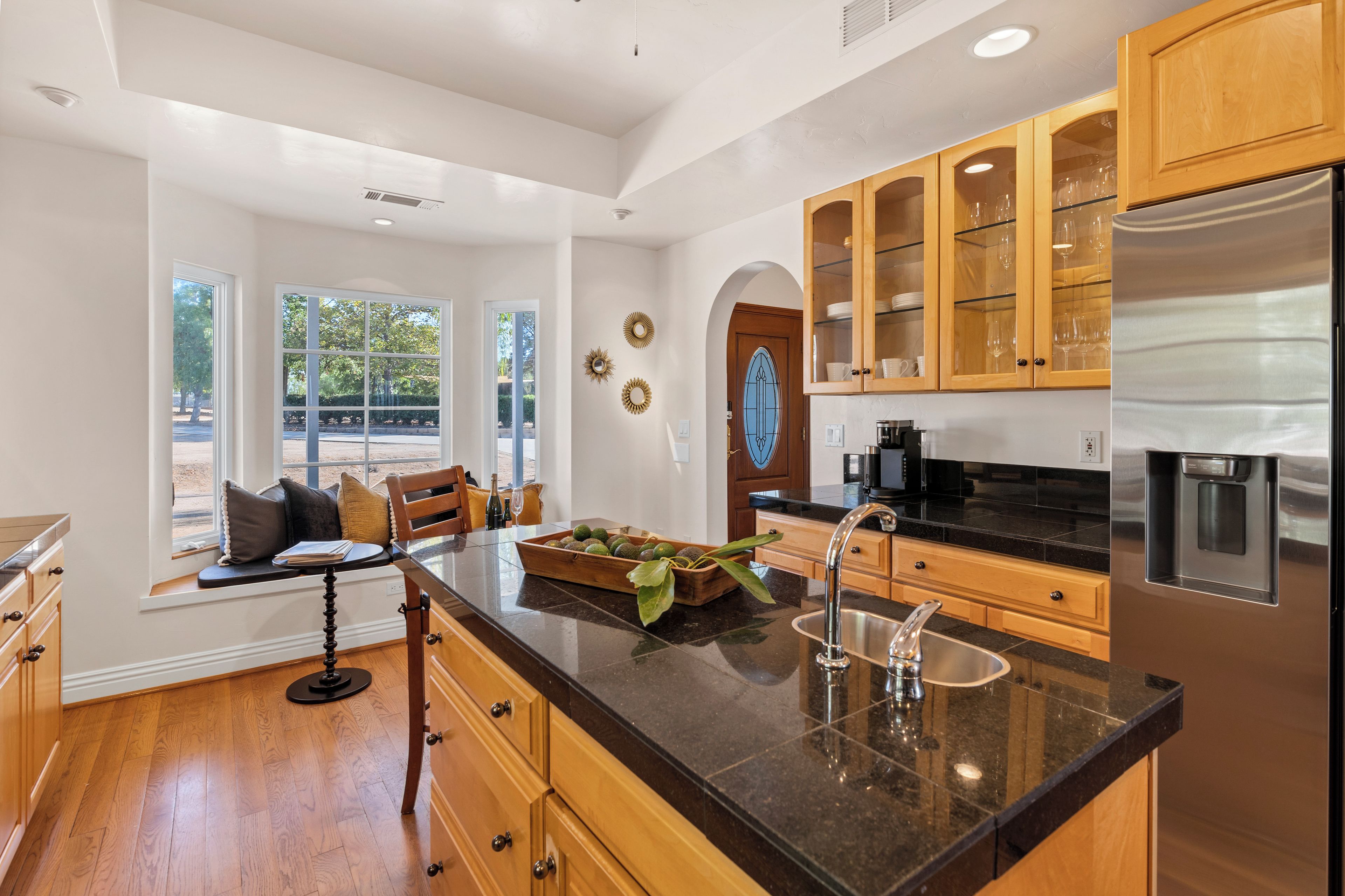 A modern kitchen with wooden cabinets, a stainless steel refrigerator, and a large window overlooking a garden.
