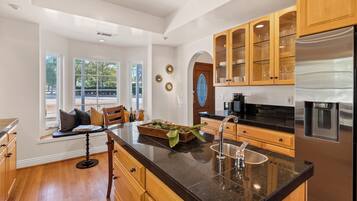 A modern kitchen with wooden cabinets, a stainless steel refrigerator, and a large window overlooking a garden.