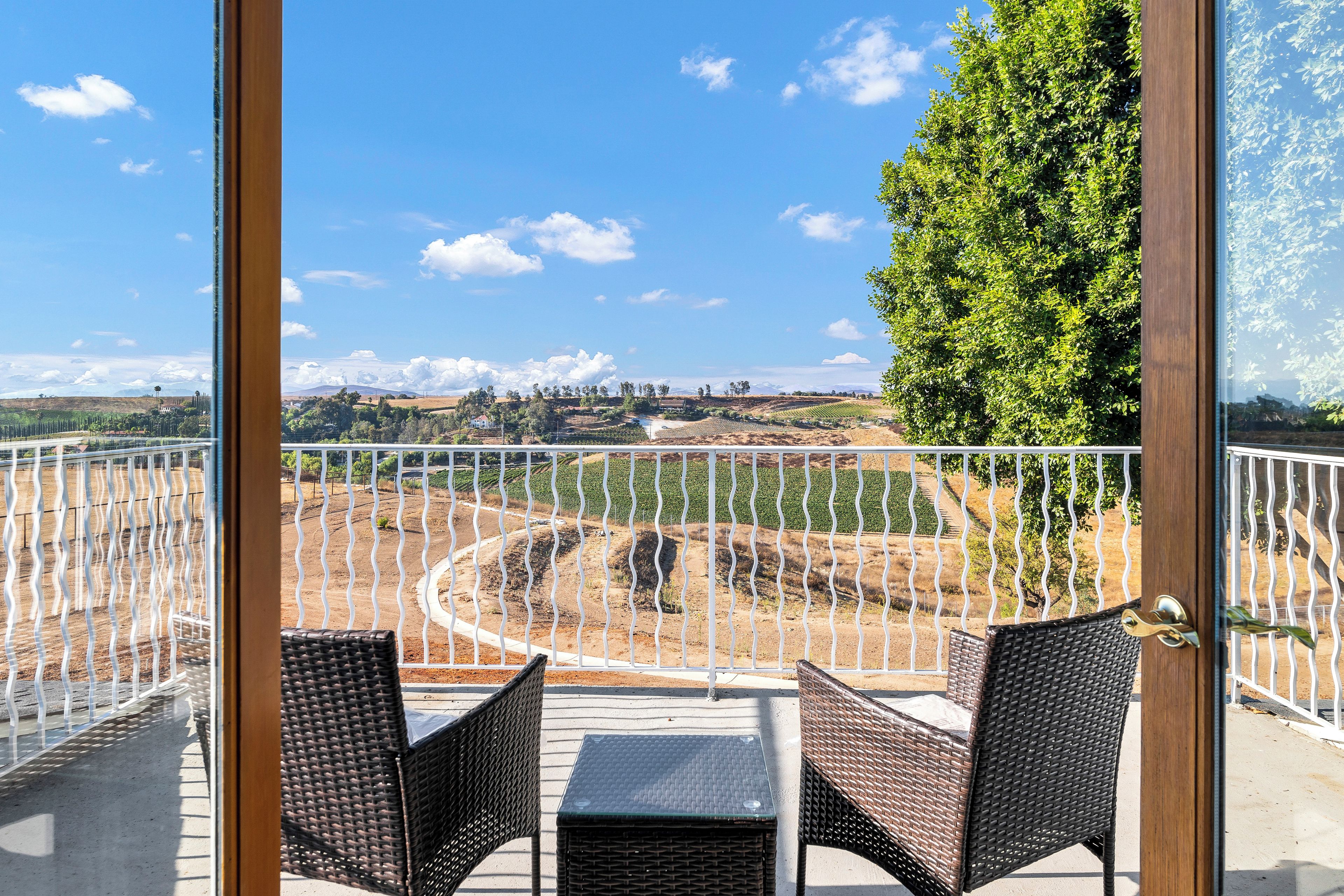 A balcony with wicker furniture and a view of a landscaped area with trees and a distant landscape.