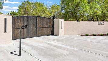 A gated entrance with a metal gate, a concrete driveway, and a wall with a number and text.
