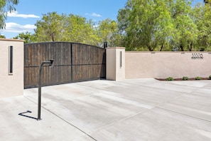 A gated entrance with a metal gate, a concrete driveway, and a wall with a number and text.