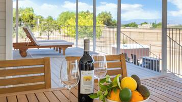 A table with a bottle of Callaway wine, two glasses, and a bowl of fruit on a wooden deck.