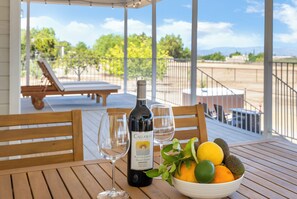 A table with a bottle of Callaway wine, two glasses, and a bowl of fruit on a wooden deck.