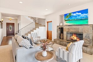 A living room with a fireplace, a staircase, and a large painting of a beach scene.