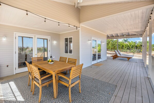 A covered patio with a wooden table and chairs, a patterned rug, and a lounge chair.